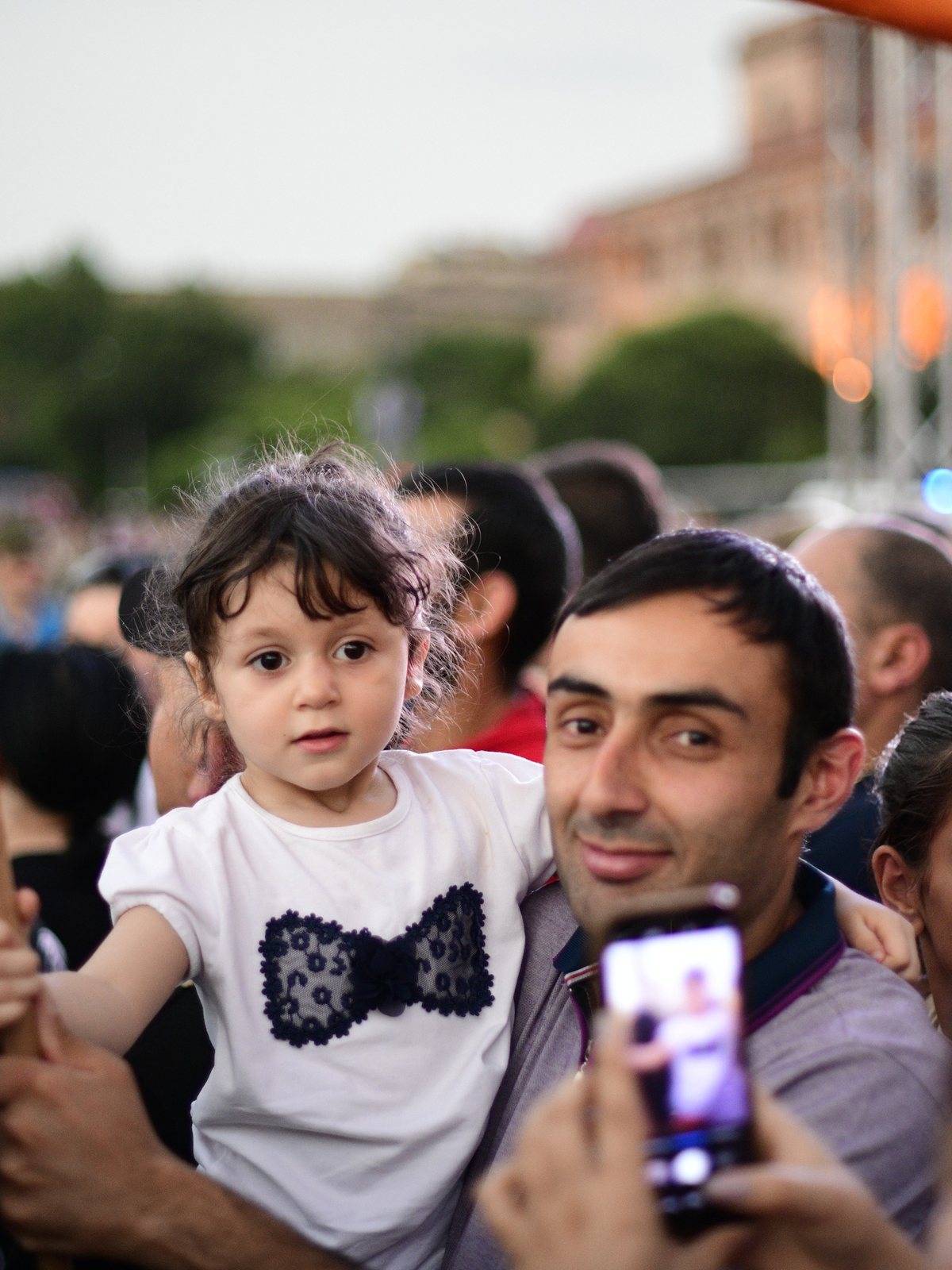 A small girl held up in the crowd beside her father, Yerevan
