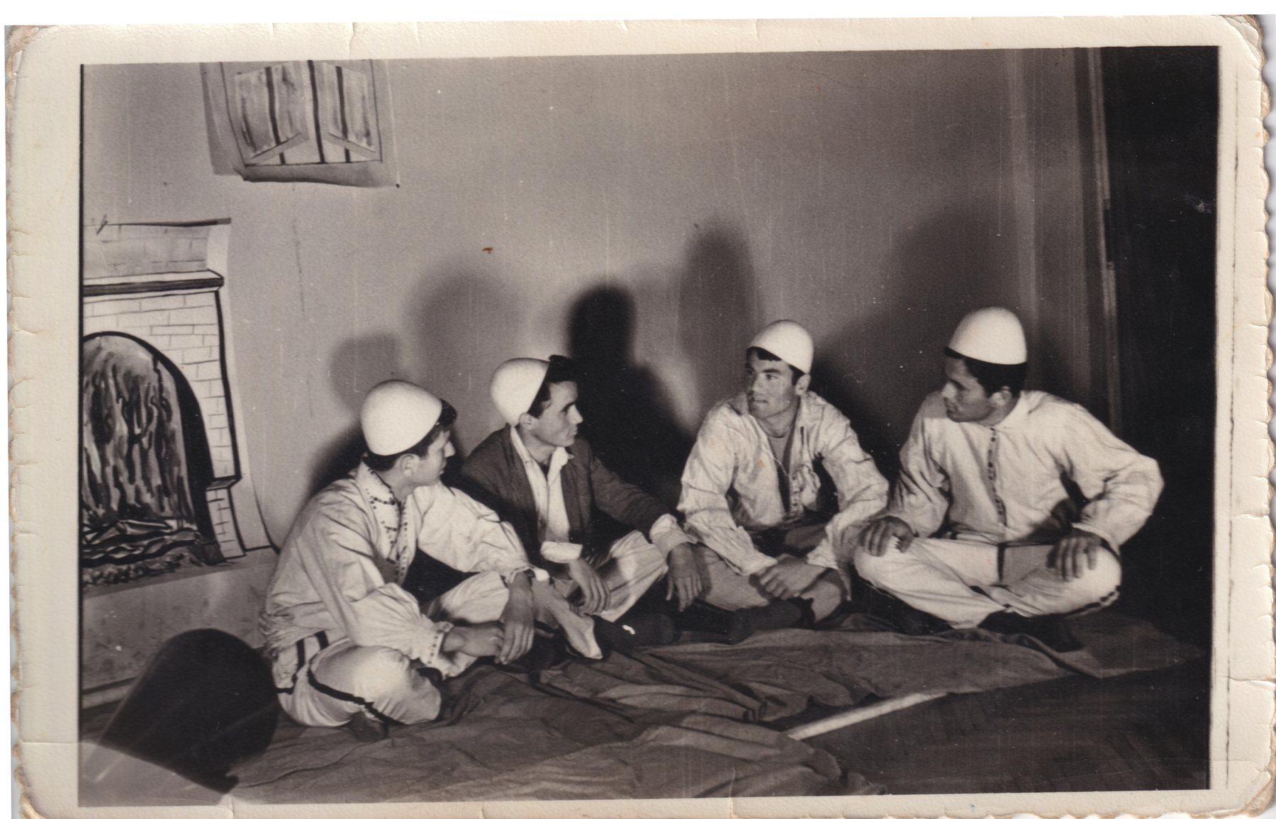 Four young men in white felt caps sit cross-legged on the floor