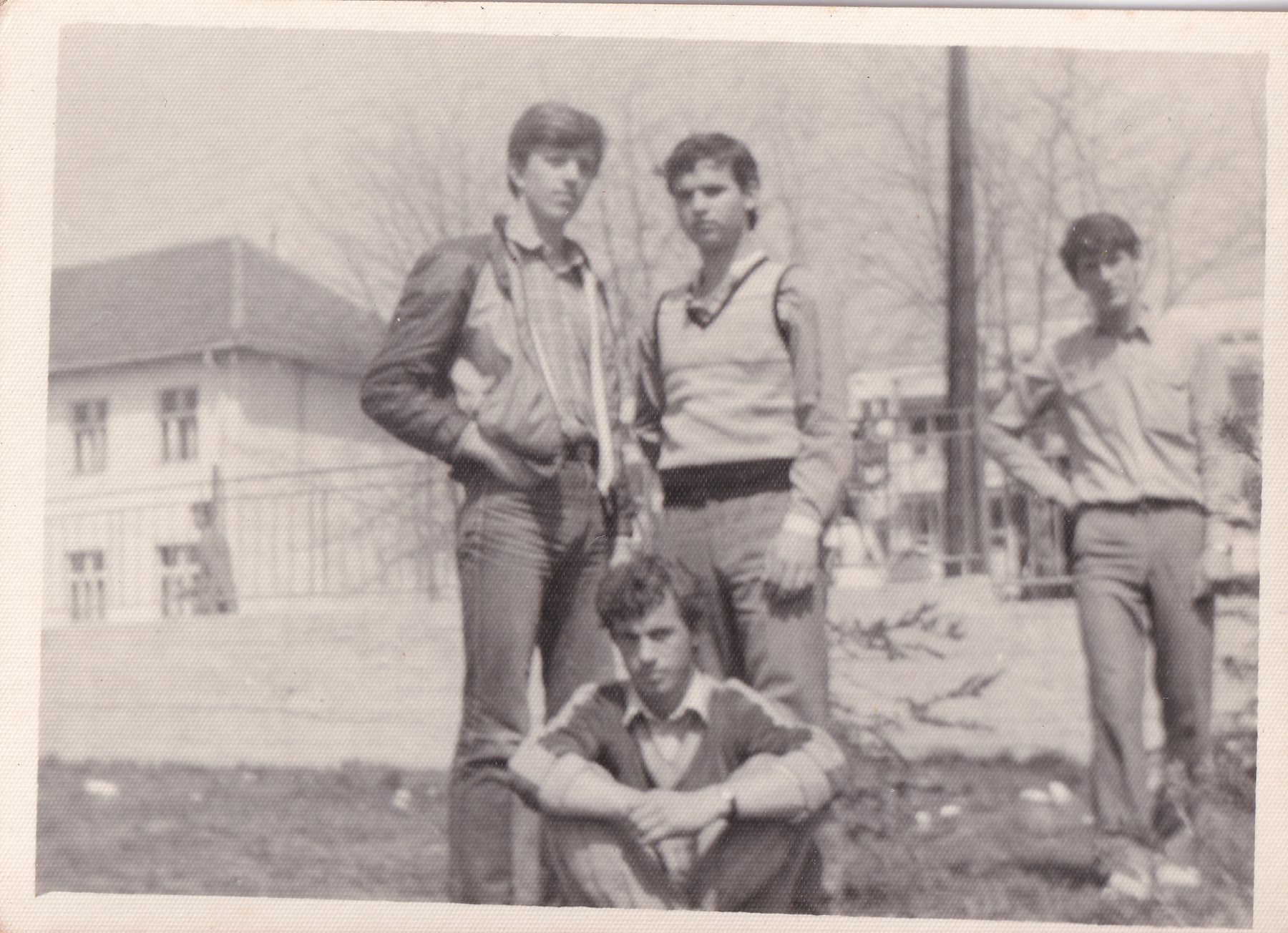Five young men in jeans pose outside a school building