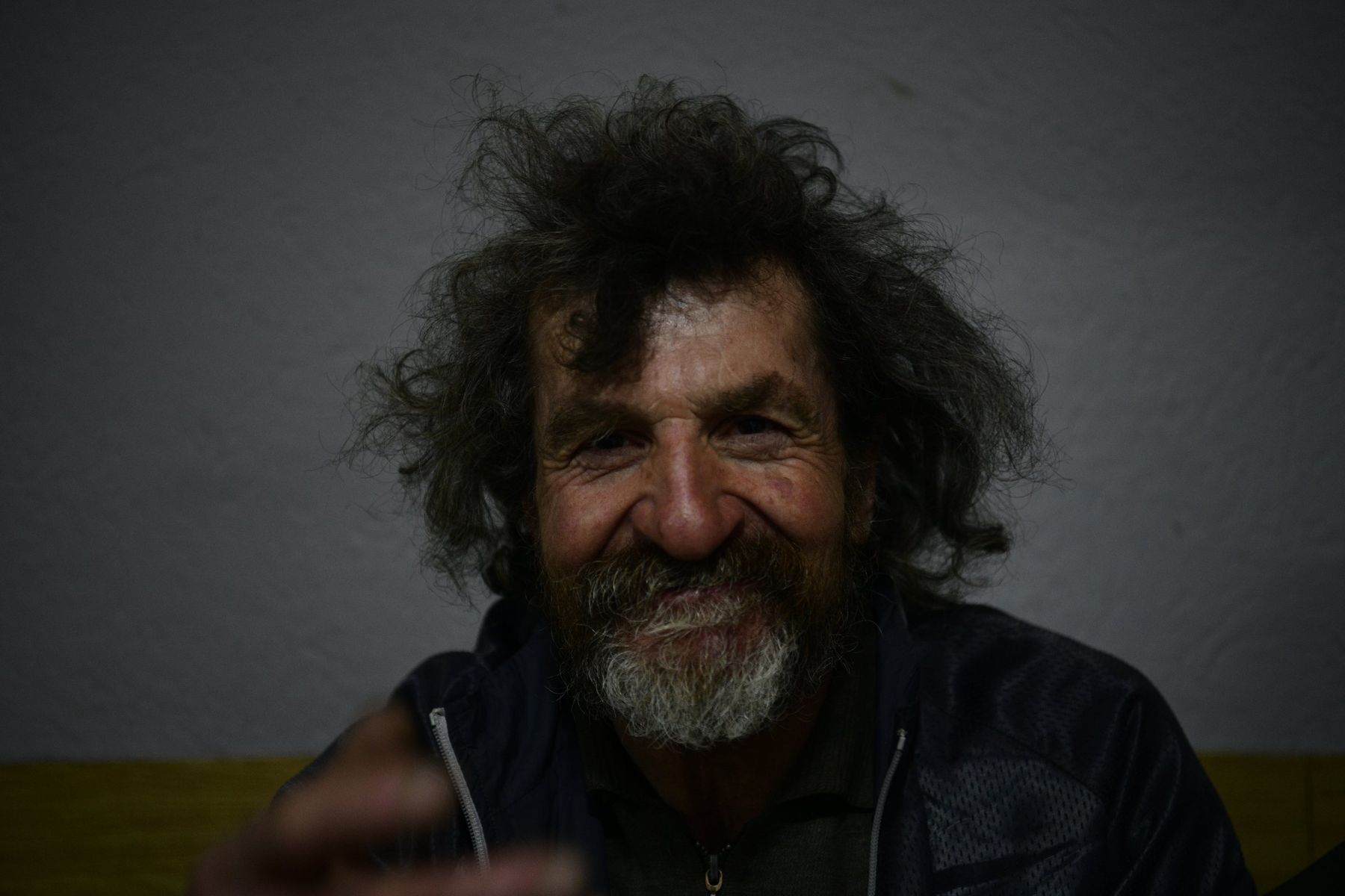 A man with wild grey hair laughs into the camera, Kosovo