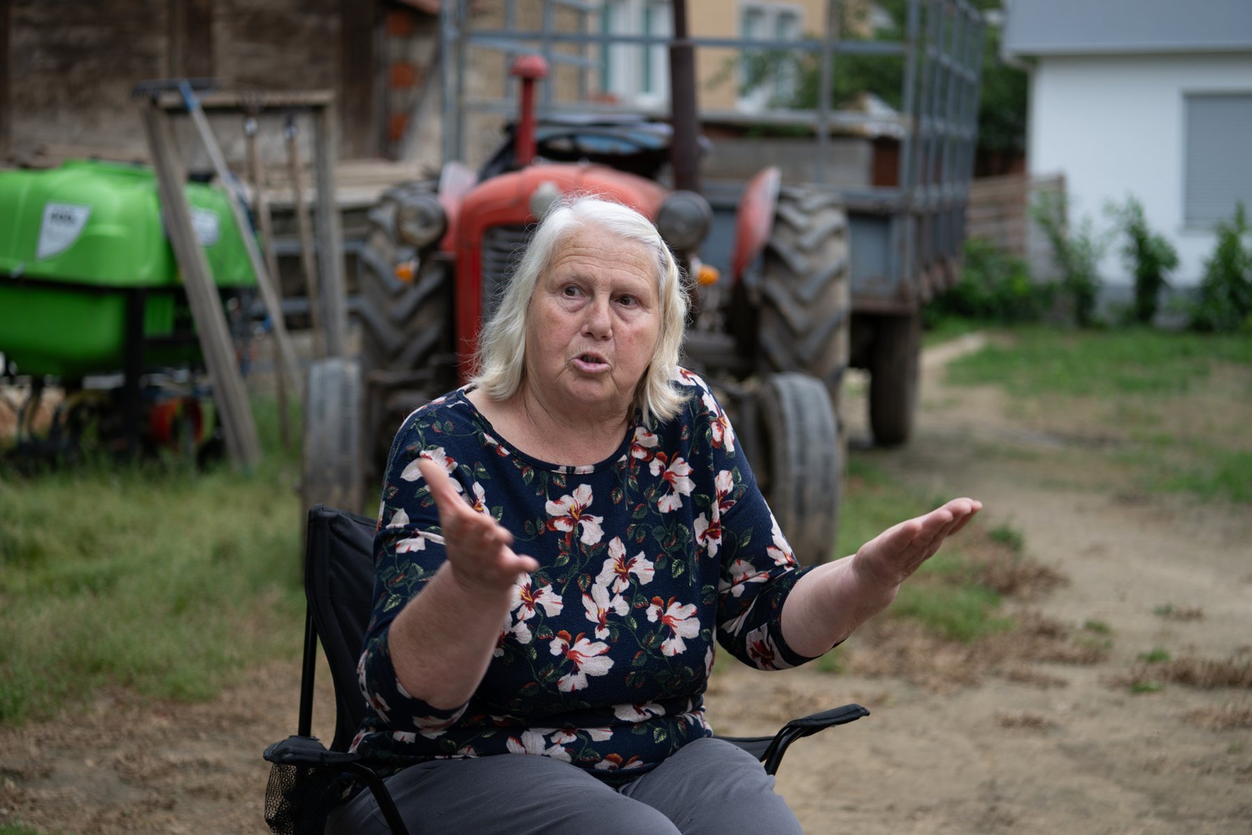 An elderly woman in a floral blouse speaks with her hands, Kosovo
