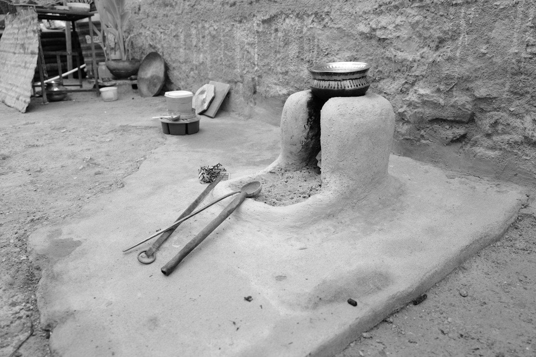 A clay stove and firewood against a stone courtyard wall