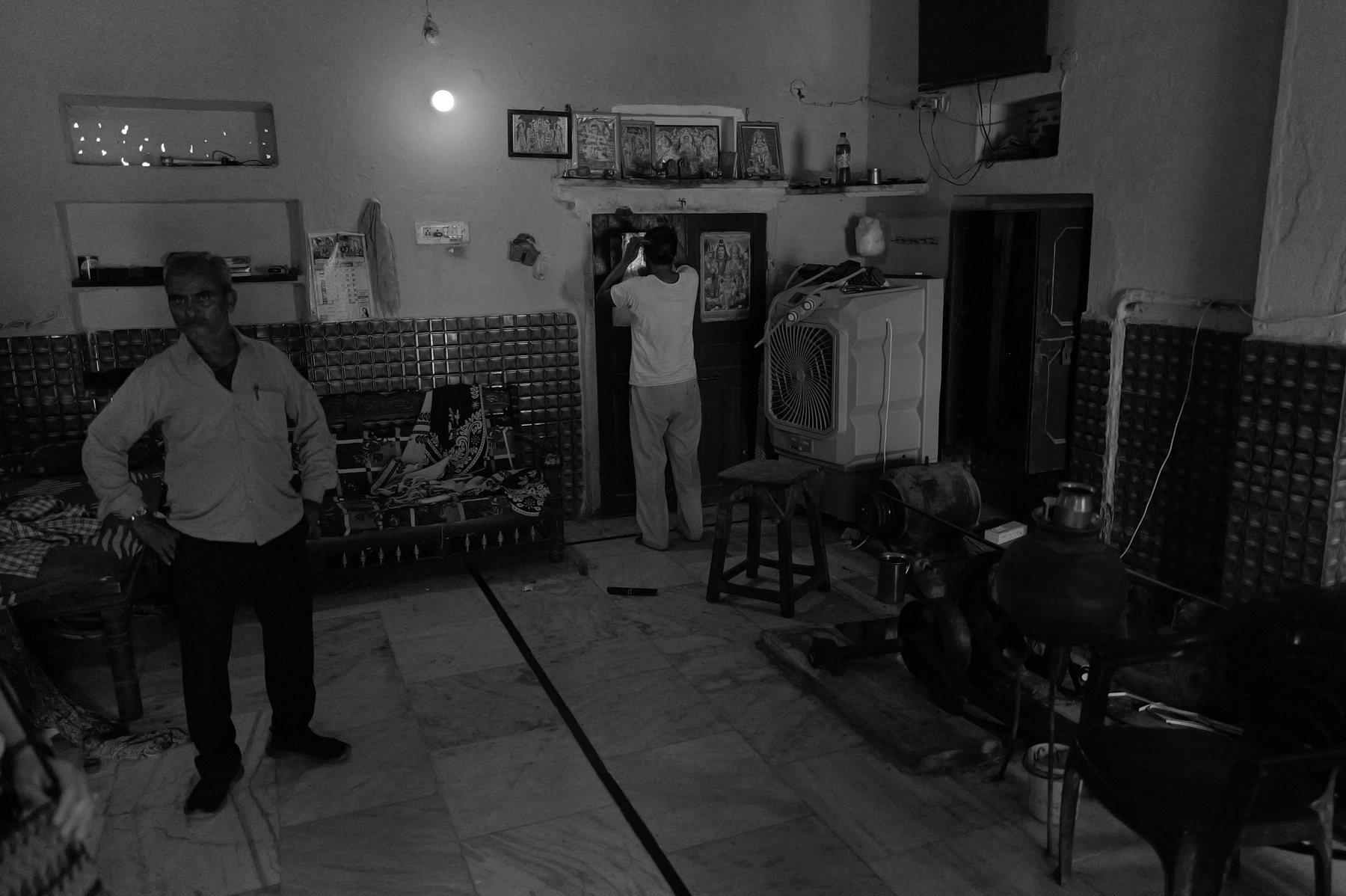 A tiled room with framed pictures of gods above a doorway, a man standing at the door