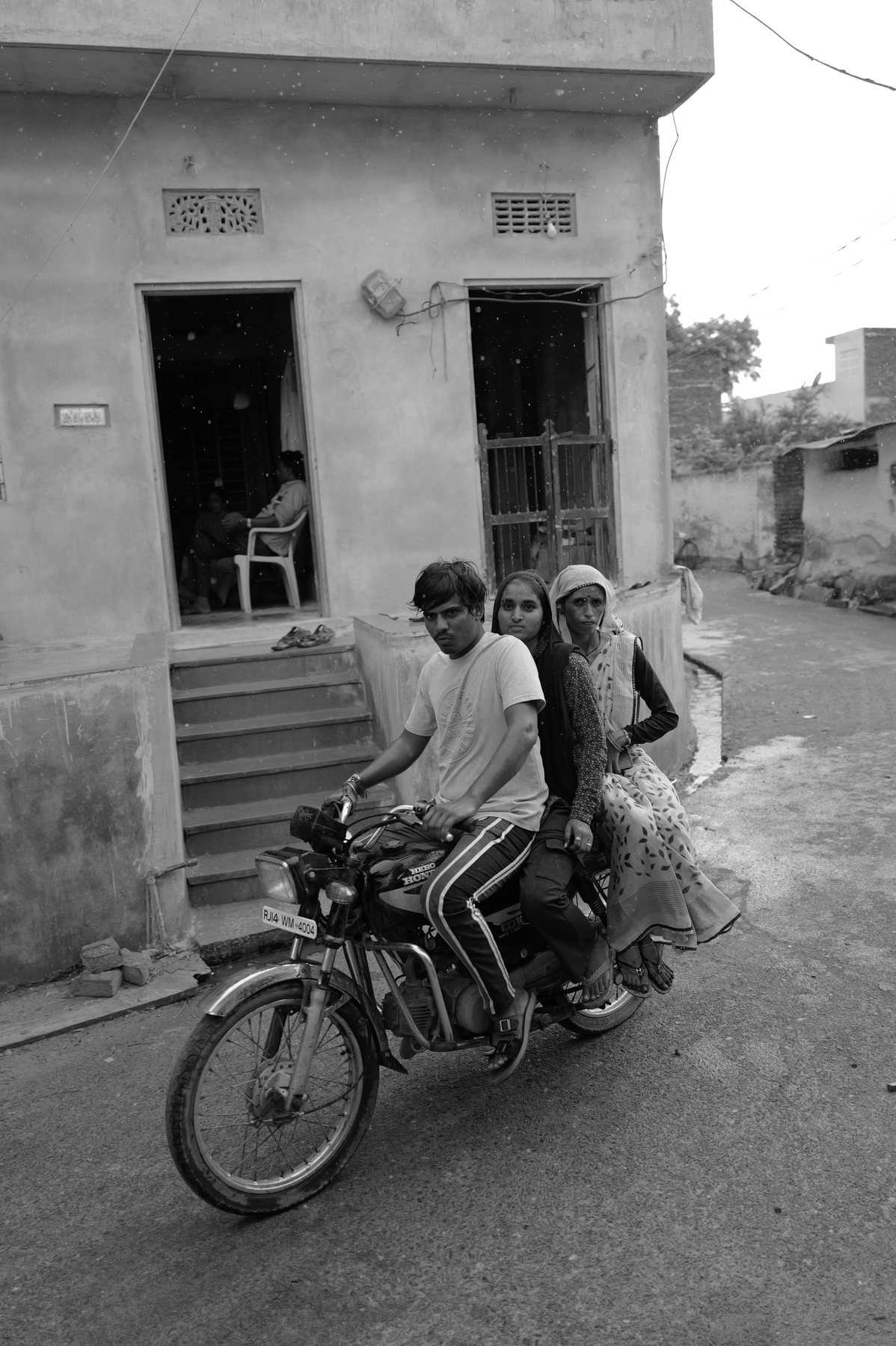 Two men ride a motorbike out of a narrow lane between houses