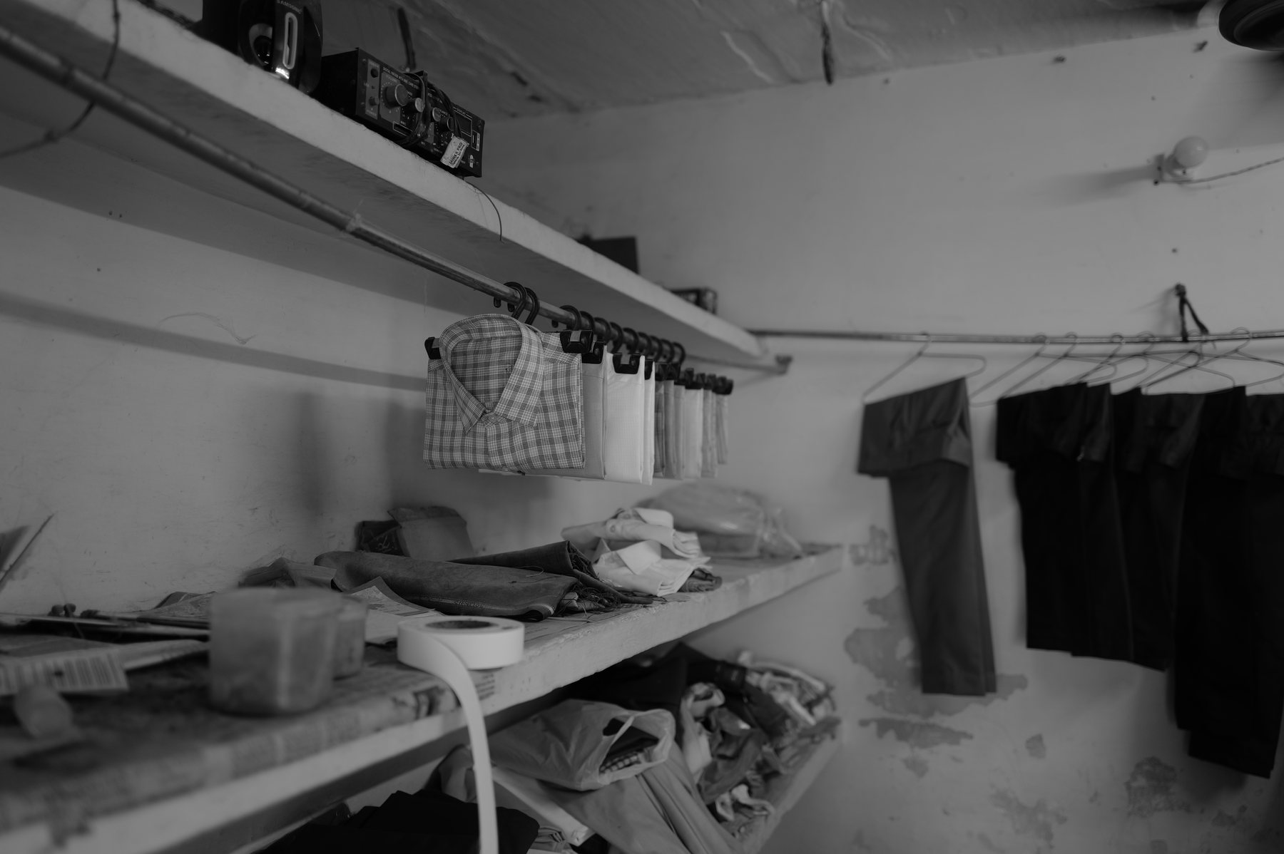 Finished shirts and trousers hang from a rail in a whitewashed room