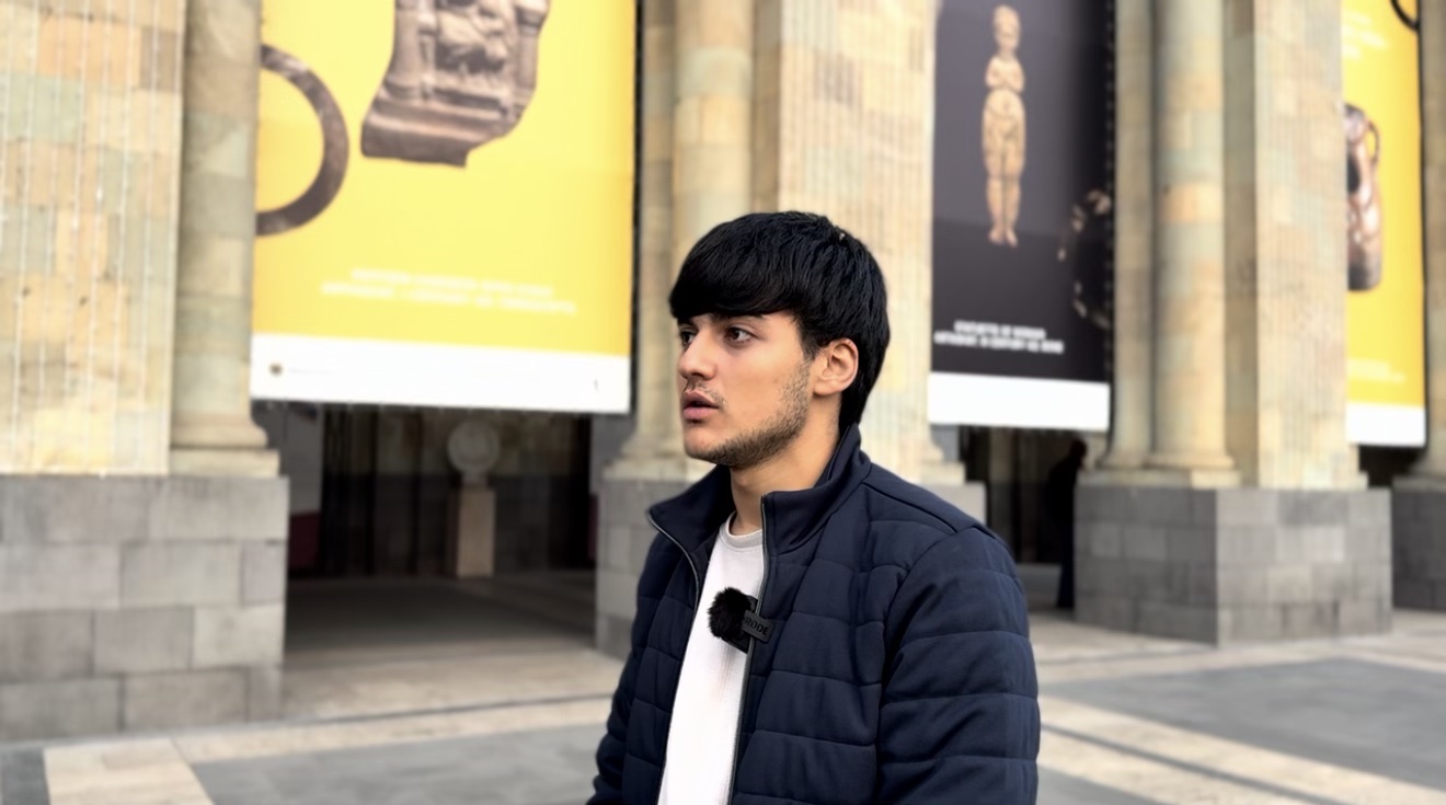 A young man in a navy jacket speaks during an interview outside a museum in Yerevan